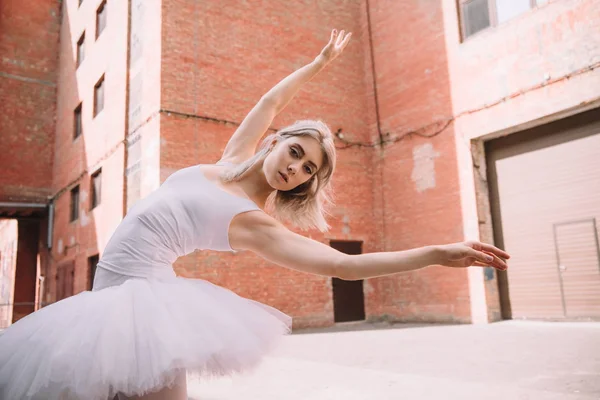 Low angle view of young ballerina looking at camera while dancing on street — Stock Photo