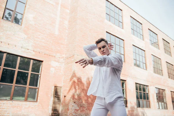 Vue de bas angle du jeune danseur masculin en vêtements blancs dansant dans la rue — Photo de stock