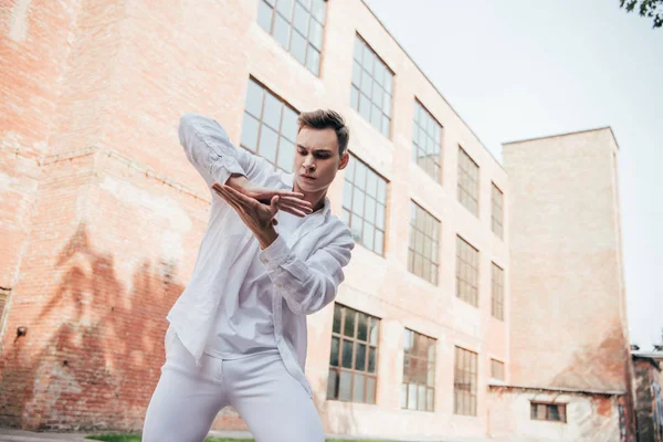 Low angle view of handsome young man in white clothes dancing on street — Stock Photo