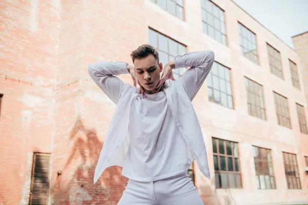 Low angle view of handsome young man in white clothes dancing on urban street — Stock Photo