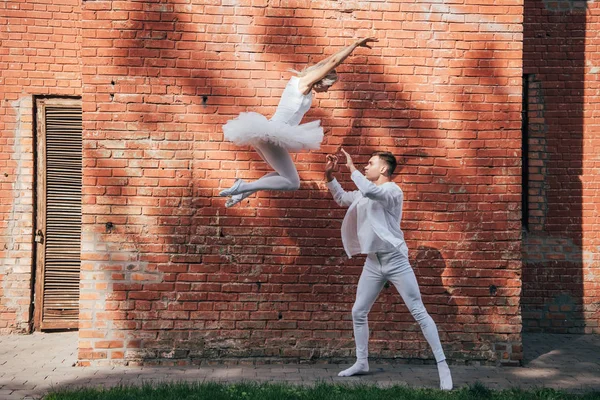 Вид сбоку красивой молодой пары танцоров, исполняющих танец балет на городской улице — стоковое фото