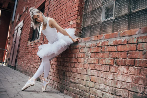 Belle jeune ballerine penché au mur de briques et regardant loin — Photo de stock