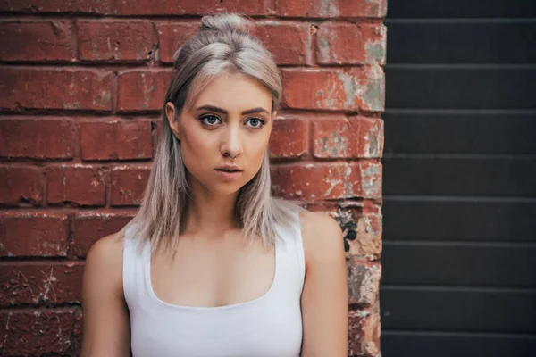 Portrait of beautiful blonde girl standing near brick wall on street — Stock Photo