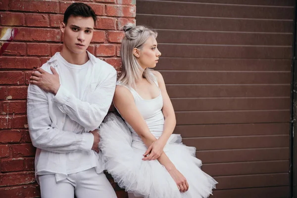 Pareja de jóvenes bailarines de pie juntos cerca de la pared de ladrillo en la calle - foto de stock