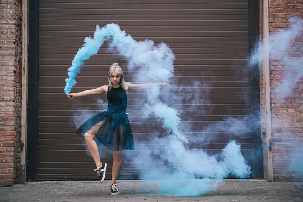 Дівчина танцює в блакитному димі і дивиться на камеру на міській вулиці міста — стокове фото
