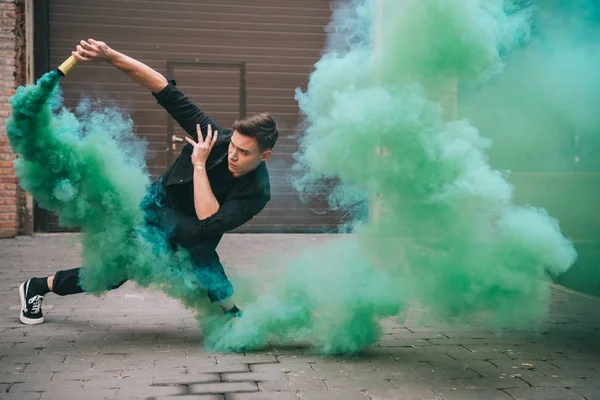 Handsome young male dancer in green smoke on street — Stock Photo