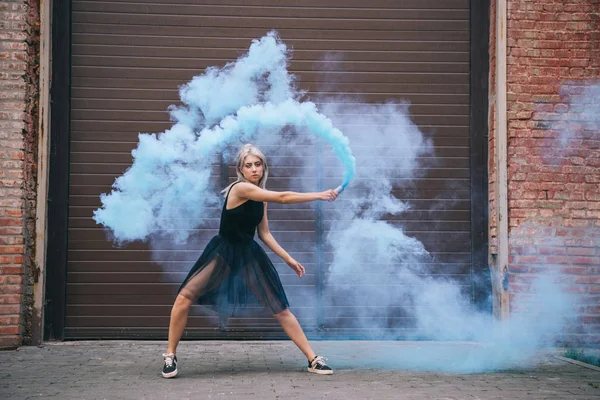 Jolie fille regardant la caméra et dansant dans la fumée bleue sur la rue — Photo de stock