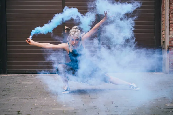 Joven bailarina contemporánea mirando a la cámara y bailando en humo azul en la calle - foto de stock