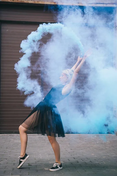 Vue latérale de la jeune femme dansant dans la fumée bleue sur la rue — Photo de stock