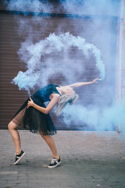 Vue latérale d'une jeune danseuse dansant dans la fumée bleue dans la rue — Photo de stock