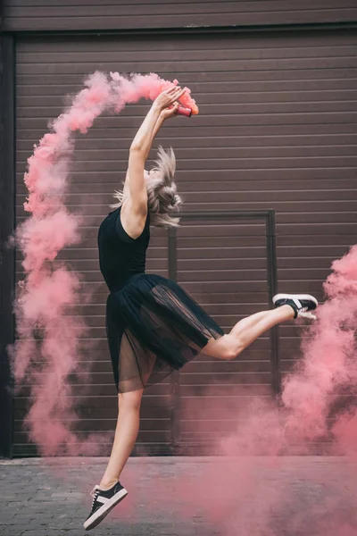 Вид збоку молодої жінки танцює в рожевому димі на вулиці — стокове фото