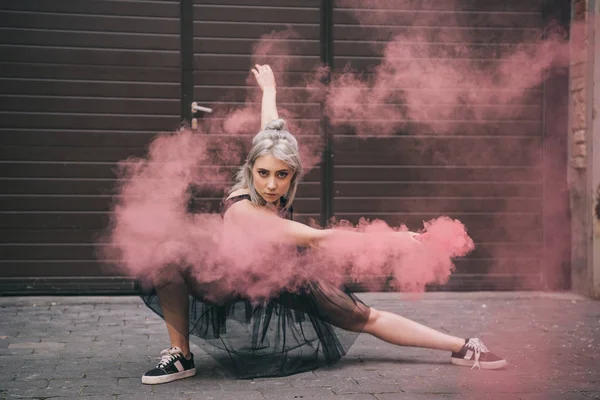 Schönes Mädchen, das in rosa Rauch tanzt und auf der Straße in die Kamera schaut — Stockfoto