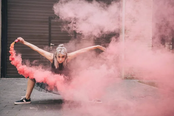 Chica atractiva mirando a la cámara mientras baila en humo rosa en la calle - foto de stock