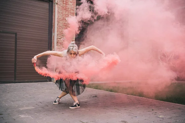 Attractive young female dancer dancing in pink smoke on street — Stock Photo