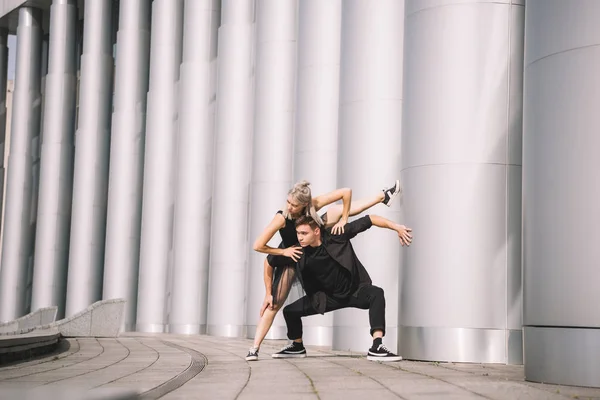 Schöne junge Darsteller in schwarzen Kleidern tanzen in der Nähe von Kolonnen auf der Straße — Stockfoto