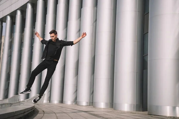 Beau jeune homme en vêtements noirs sautant en danse sur la rue — Photo de stock