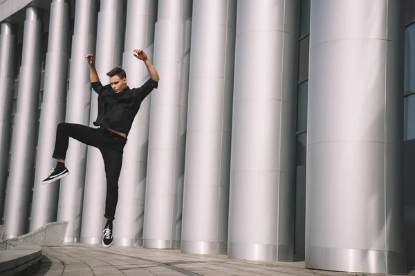 Schöner junger Mann in schwarzer Kleidung tanzt und springt in der Nähe von Säulen — Stockfoto