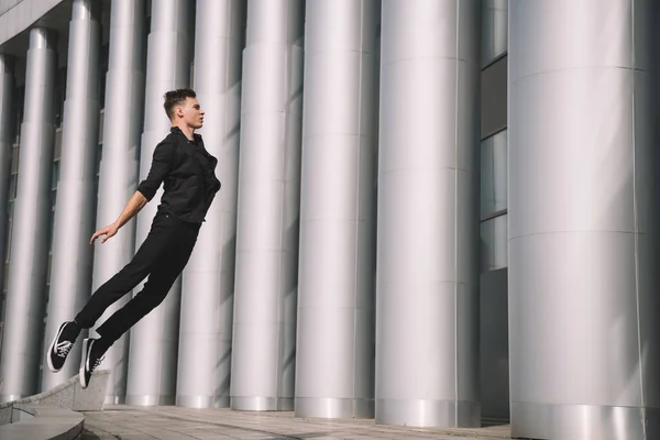 Молодий чоловік танцюрист в чорному одязі стрибає на вулиці — стокове фото