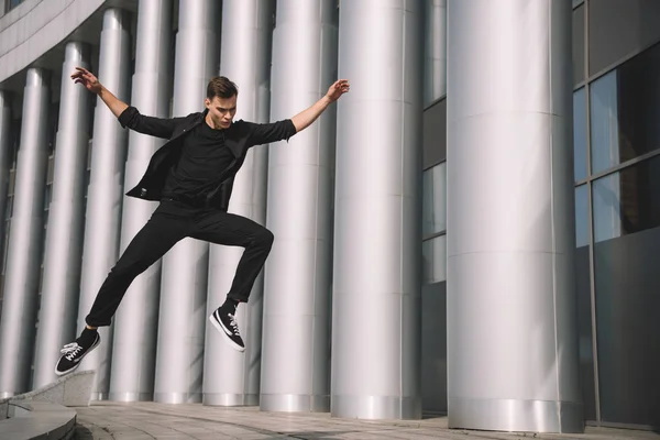 Joven guapo en ropa negra saltando y bailando en la calle - foto de stock