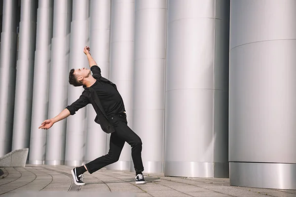 Молодий чоловік в чорному одязі танцює біля колон на вулиці — стокове фото
