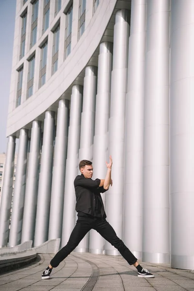 Молодий чоловік танцюрист в чорному одязі біля колон на вулиці — стокове фото
