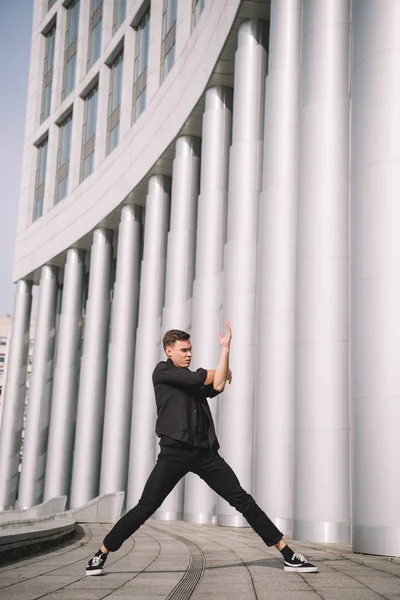 Giovane ballerino in abiti neri vicino a colonne sulla strada — Foto stock