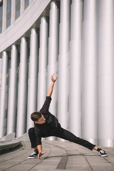 Schöner junger Mann in schwarzer Kleidung tanzt in der Nähe von Säulen — Stockfoto