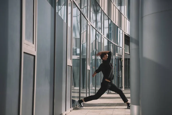 Joven con ropa negra bailando cerca de columnas - foto de stock