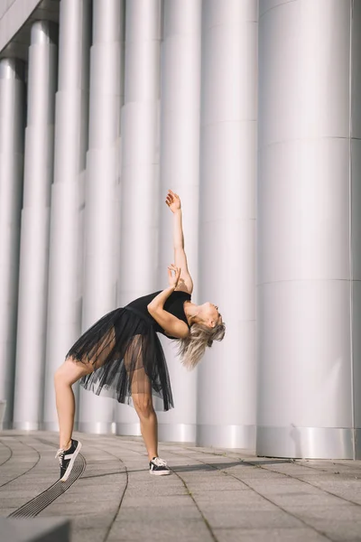 Beautiful girl in black skirt dancing near columns on street — Stock Photo