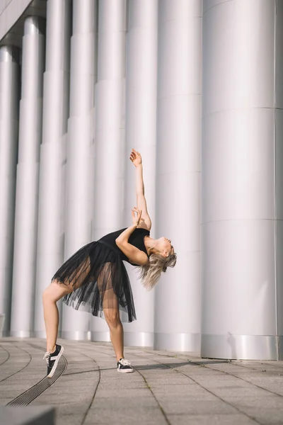 Hermosa chica en negro falda bailando cerca de columnas en la calle - foto de stock