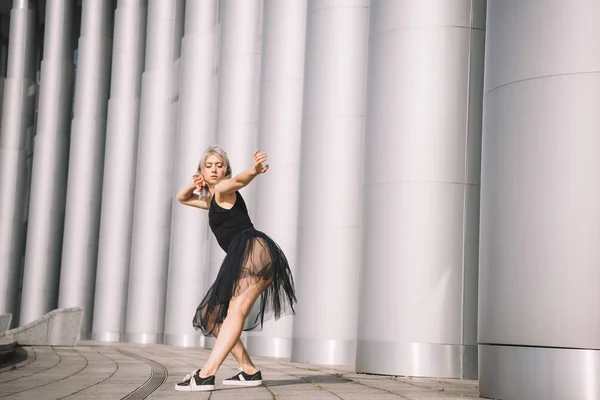 Side view of beautiful young dancer in black skirt near columns on street — Stock Photo