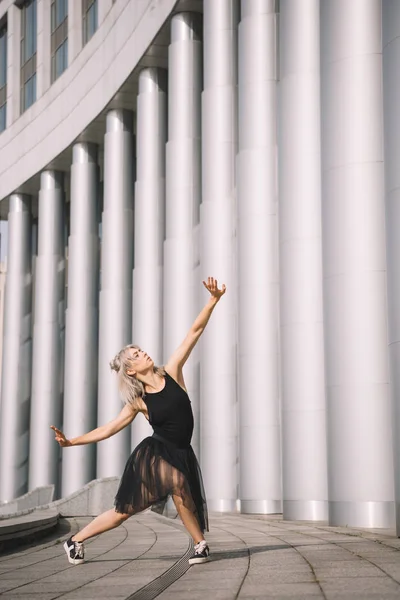 Attractive girl in black skirt dancing near columns on street — Stock Photo