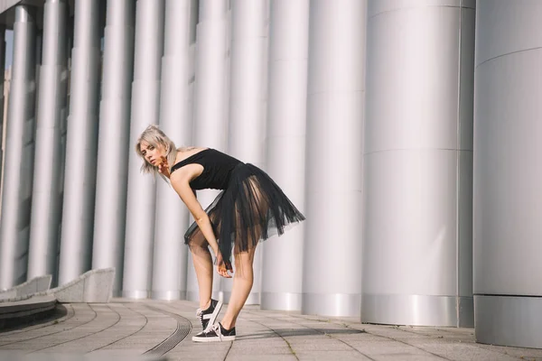 Seitenansicht der jungen Ballerina im schwarzen Rock, die auf der Straße in die Kamera schaut — Stockfoto