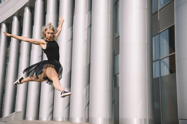 Low angle view of young ballerina jumping and dancing on street — Stock Photo