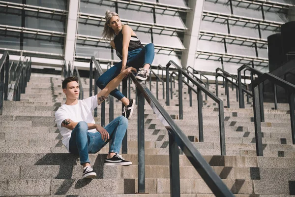 Stylish sporty young couple with backpacks sitting on stairs and railings — Stock Photo