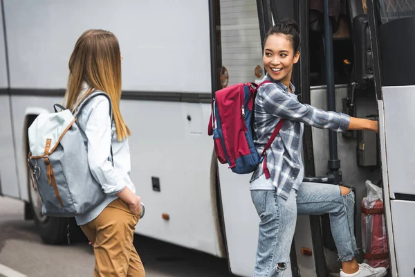 Multicultural female travelers with backpacks walking into travel bus at street — Stock Photo
