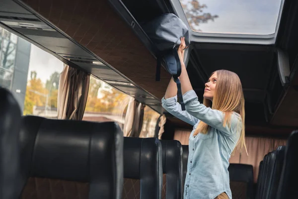 Selective focus of female tourist putting backpack on shelf in travel bus — Stock Photo