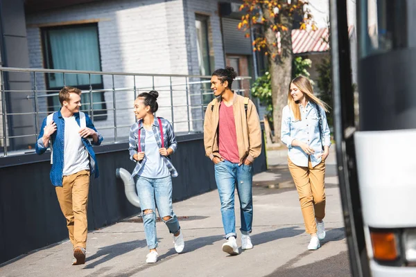 Fröhliche junge Freunde mit Rucksäcken laufen in der Nähe des Reisebusses an der Stadtstraße — Stockfoto