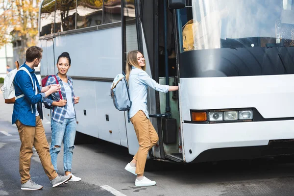 Selective focus of multiethnic tourists with backpacks walking into travel bus at city street — Stock Photo