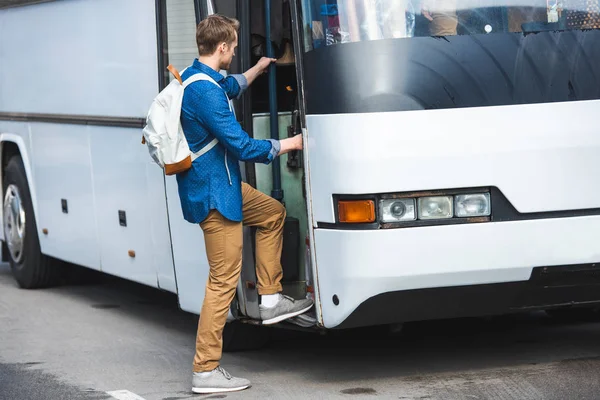 Seitenansicht eines männlichen Touristen mit Rucksack, der auf der Straße in einen Reisebus einsteigt — Stockfoto