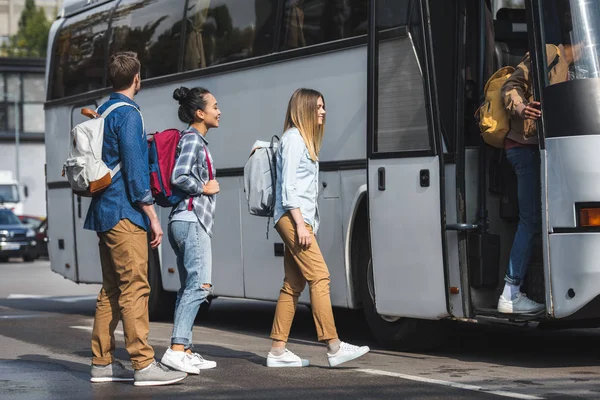 Молоді усміхнені туристи з рюкзаками, що йдуть в туристичний автобус на міській вулиці — стокове фото