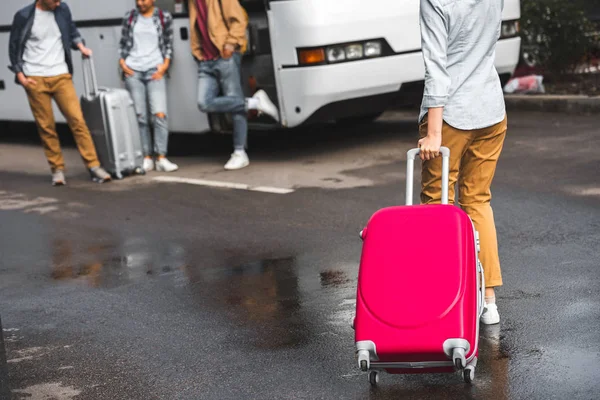 Image recadrée d'une femme portant un sac à roulettes tandis que ses amis attendent près d'un bus de voyage dans une rue urbaine — Photo de stock