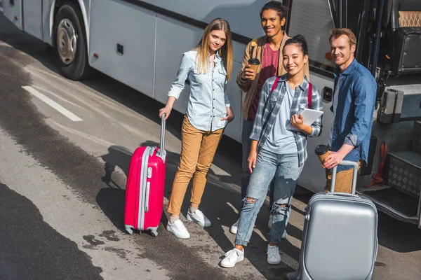 Vista ad alto angolo di amici multietnici con borse a ruote in posa vicino autobus di viaggio in strada della città — Foto stock