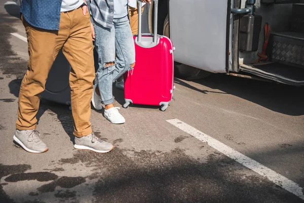 Обрізане зображення друзів з колісними сумками, що йдуть біля туристичного автобуса на вулиці — стокове фото