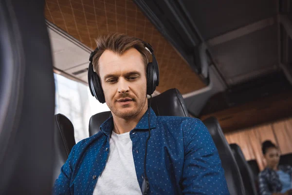 Дорослий чоловік в навушниках слухає музику і дивиться вниз під час поїздки на туристичному автобусі — стокове фото
