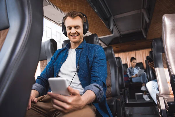 Homem adulto feliz em fones de ouvido ouvindo música e usando smartphone durante a viagem no ônibus — Fotografia de Stock