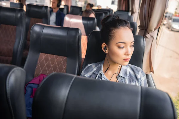 Schöne asiatische Frau hört Musik in Kopfhörern während der Reise im Reisebus — Stockfoto