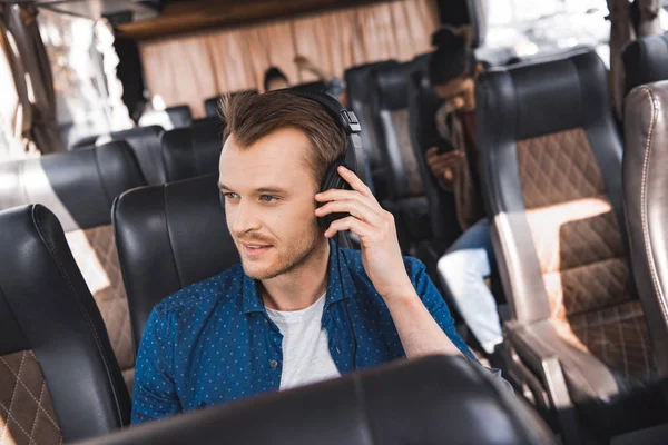 Schöner männlicher Tourist mit Kopfhörer, der Musik hört und während der Fahrt im Reisebus wegschaut — Stockfoto