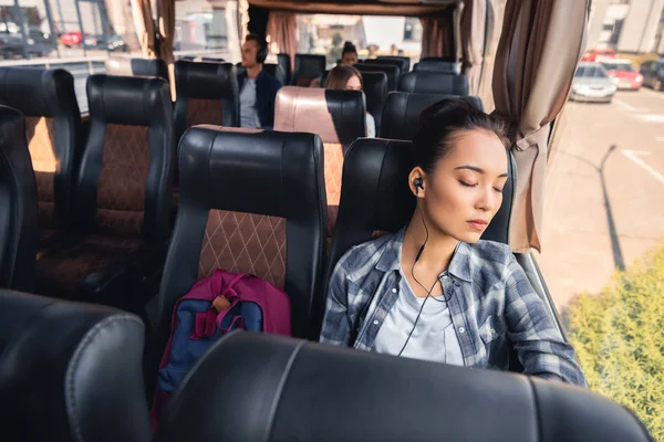 Asiática jovem mulher dormindo e ouvindo música em fones de ouvido durante viagem em ônibus de viagem — Fotografia de Stock