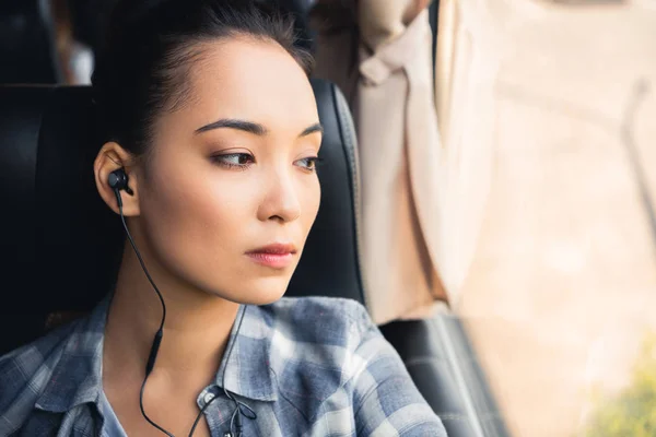 Close up portrait of asian woman listening music in earphones and looking away during trip on travel bus — Stock Photo